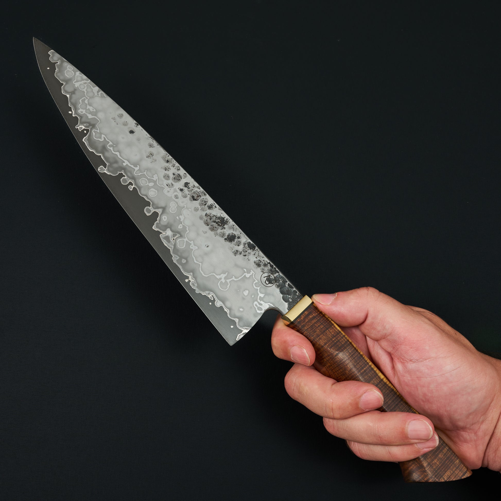 Denty stainless clad Apex Ultra blade of a Tobias Hangler 235mm chef knife, held in the hand